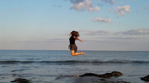 Woman jumping on beach against sky during sunset