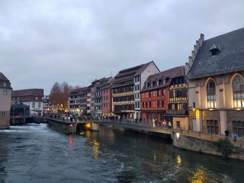 Buildings by river against cloudy sky