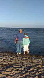 Rear view of couple standing on beach against sea