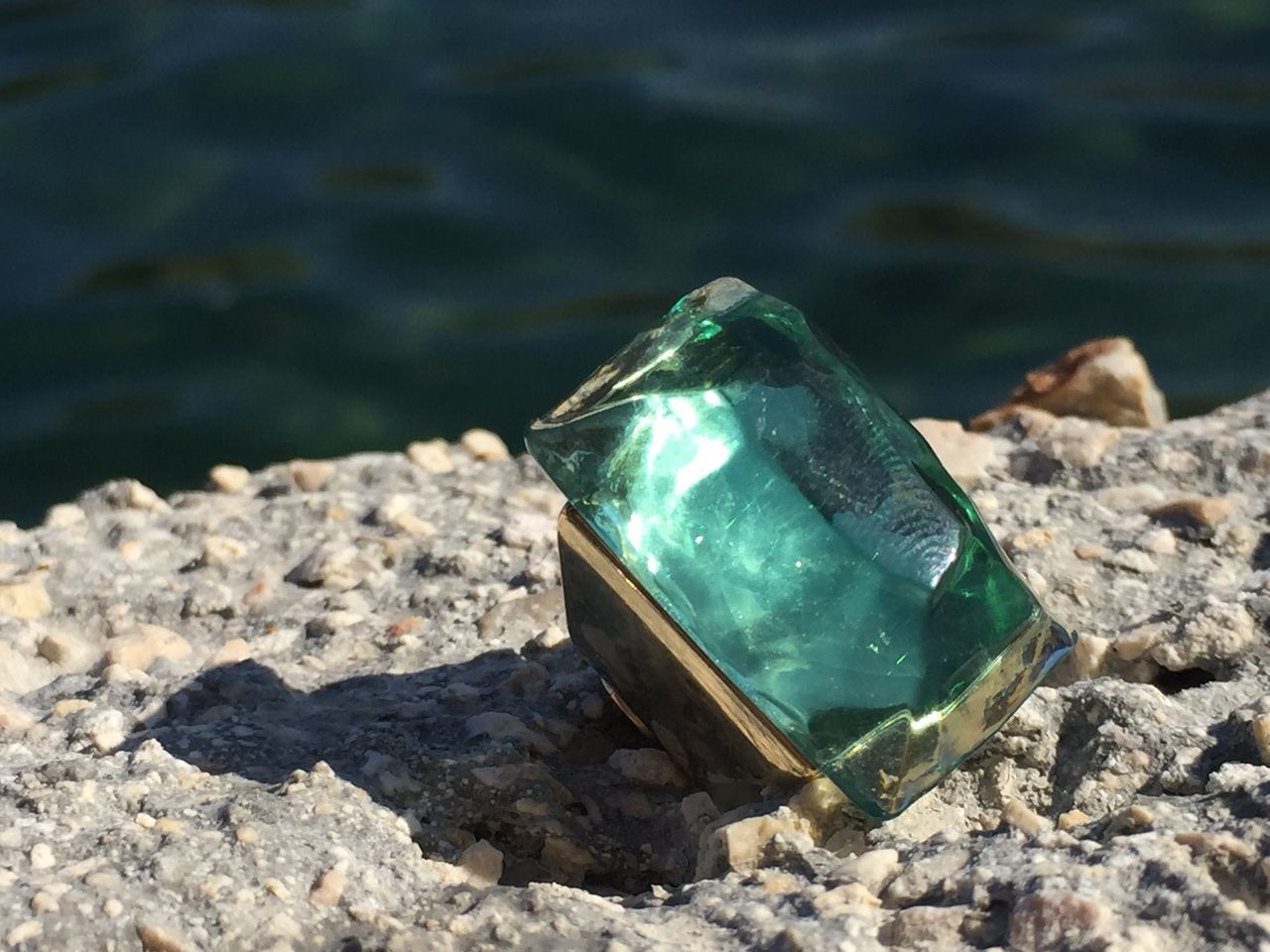 solid, water, rock, nature, sunlight, rock - object, day, green color, close-up, focus on foreground, glass - material, no people, transparent, container, stone - object, bottle, outdoors, single object, gemstone, precious gem, pollution, turquoise colored