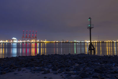 Illuminated buildings by sea against sky at night