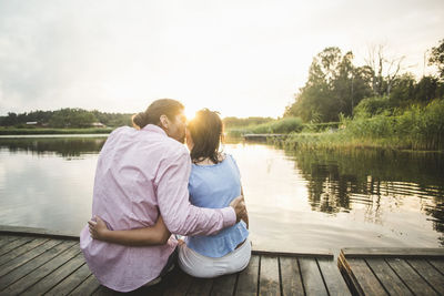 Rear view of couple sitting on lake against sky