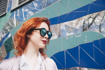 Redhead young woman wearing sunglasses against mosaic wall