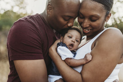 Close up happy mother and father cuddling infant girl backlit field