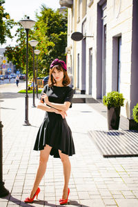 Beautiful young woman in black dress standing on sidewalk in city