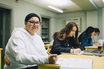 Portrait of smiling male high school student sitting by classmate in classroom