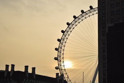 Low angle view of buildings by millennium wheel against sky during sunset
