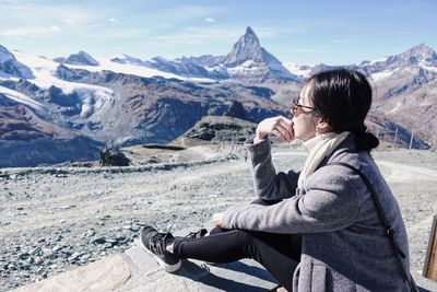 Woman sitting on snowcapped mountain against sky