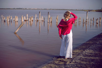 Portrait of young woman in pink and white clothes wearing sunglasses stand on pink lake 