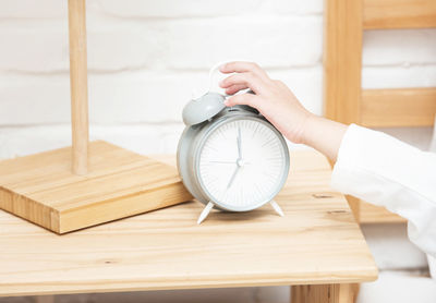 Close-up of hand holding clock on table