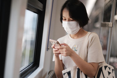 Young woman using phone by window in train