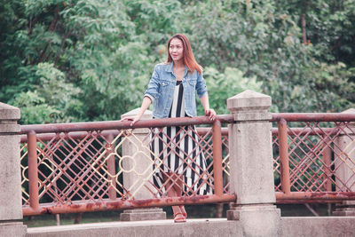 Portrait of young woman standing against railing