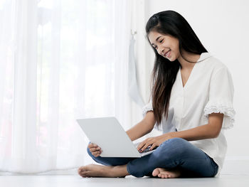 Young woman using smart phone while sitting on laptop