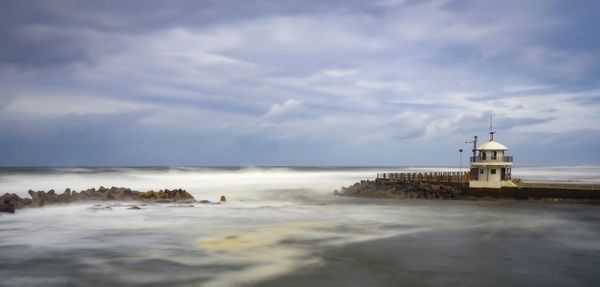 Lighthouse on beach by sea against sky