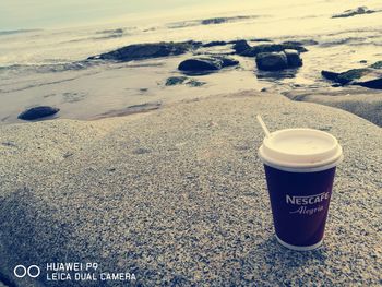 Close-up of coffee cup on sand at beach