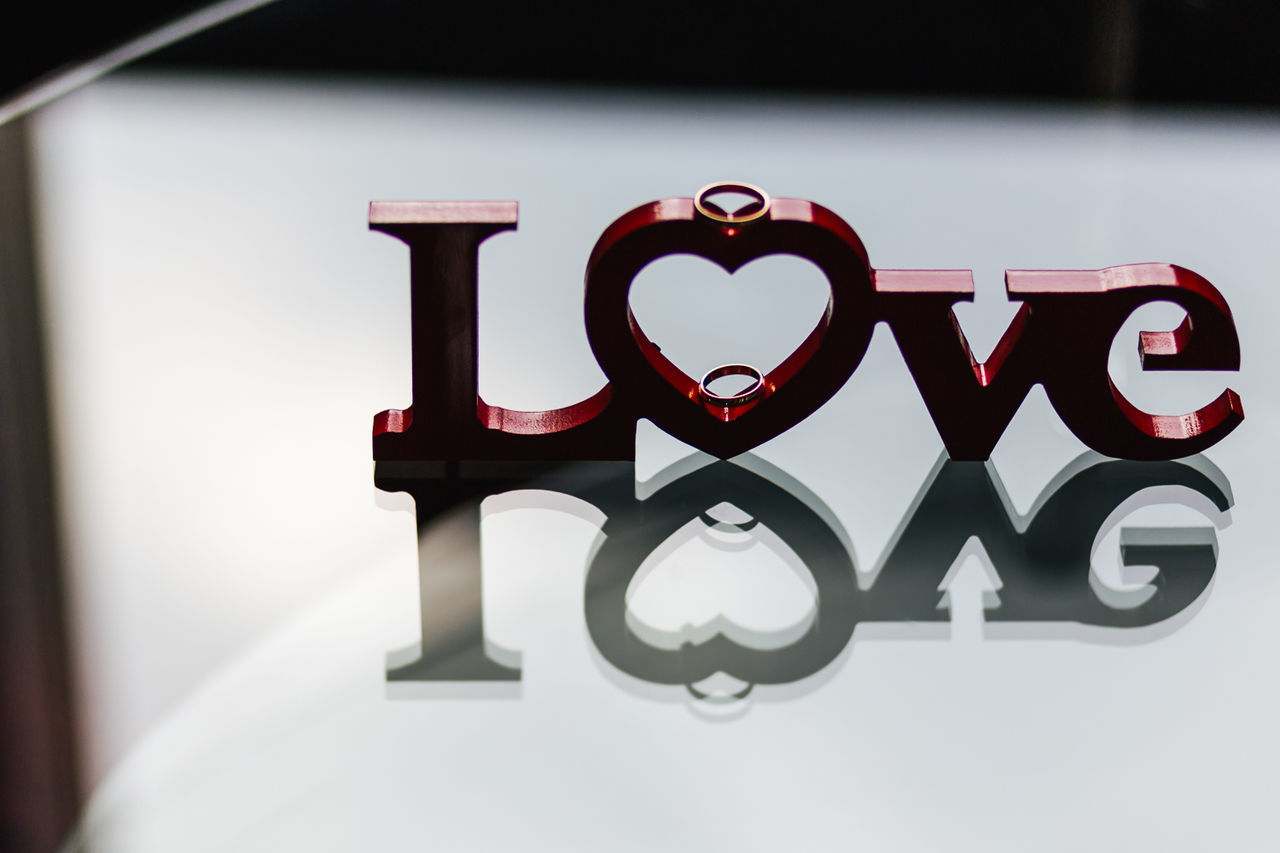 High angle view of love text with wedding rings on glass table