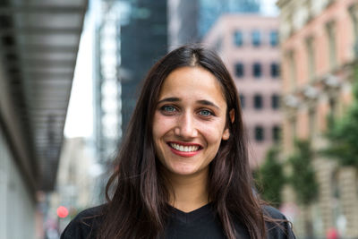 Portrait of smiling young woman standing against buildings in city