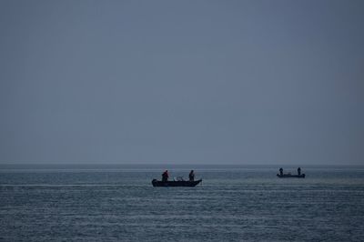 People on boats sailing in sea against clear sky