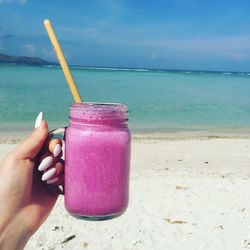 Close-up of hand holding drink at beach against sky