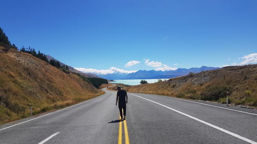 Rear view of man walking on road against clear blue sky