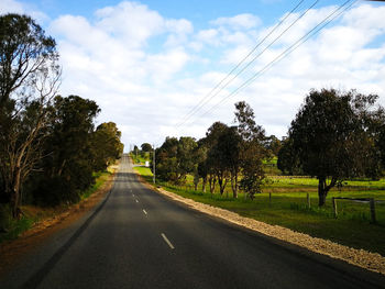 Road amidst trees on field against sky