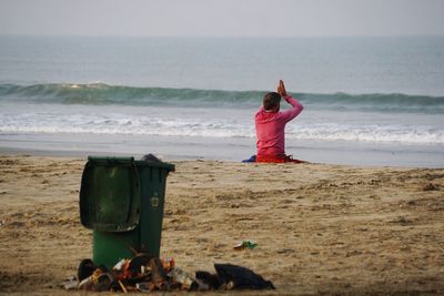 Rear view of man with hands clasped sitting at beach