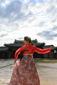 Woman in red dress dancing against gyeongbokgung during sunny day