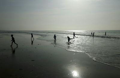 Silhouette children playing at beach against sky