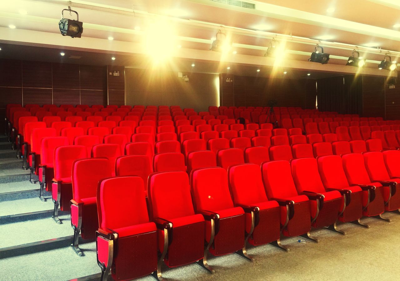 in a row, red, seat, empty, arts culture and entertainment, movie theater, indoors, auditorium, chair, no people, event, absence, stage theater, repetition, stage - performance space, lighting equipment, large group of objects, performance, stage, performing arts event, luxury, nightlife