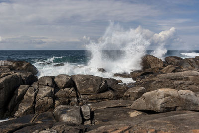 Waves splashing on rocks at shore against sky