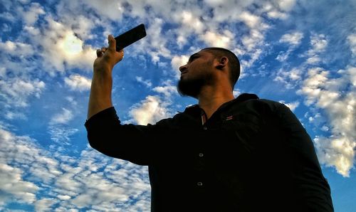 Low angle view of man holding camera against sky