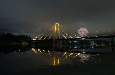 Illuminated bridge over river against sky at night