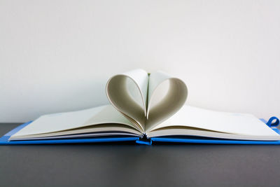 Close-up of heart shape made in book on table against gray wall