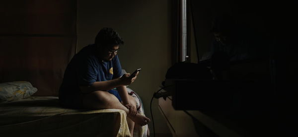 Men using mobile phone while sitting on bed at home