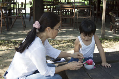 Mother assisting son in eating slush at table