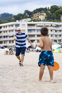 Rear view of boy playing with grandfather on beach