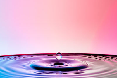 Close-up of droplet splashing in water against colored background