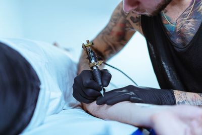 Midsection of man tattooing on customer hand