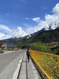 Rear view of man walking on road against sky