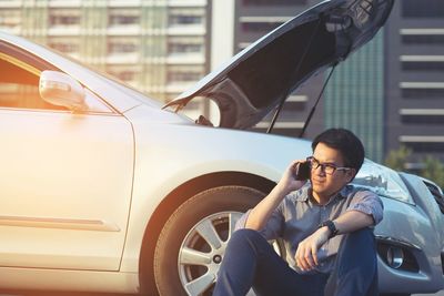 Man talking on phone while sitting by broken car