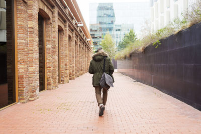 Bearded man walking across pathway holding a take away coffee