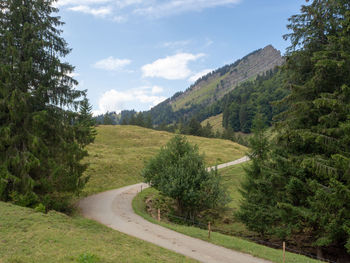 Road amidst green landscape and trees against sky