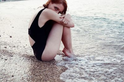 Full length side view of woman sitting on shore at beach