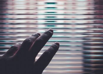 Cropped image of hand against window blinds