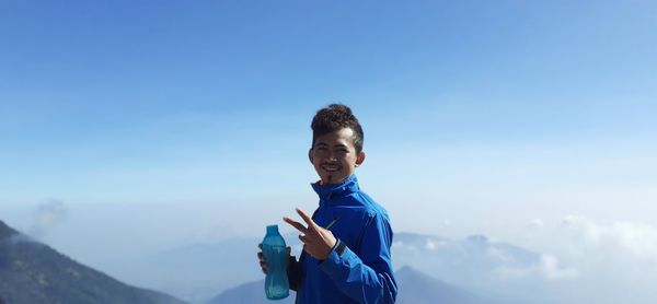 Portrait of smiling man standing on mountain against blue sky