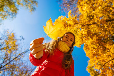 Low angle view of woman holding autumn leaves