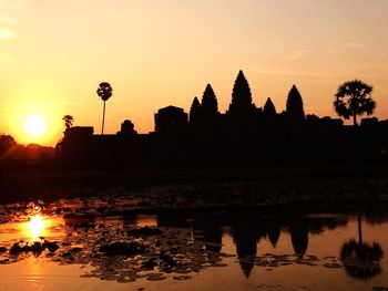 Silhouette temple by lake against sky during sunset