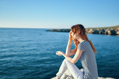 Woman sitting near sea against clear sky