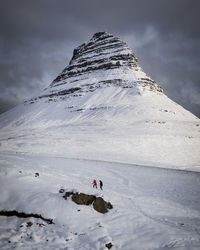 People on snowcapped mountain against cloudy sky