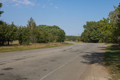 Empty road amidst trees against sky in city